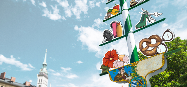 Bild von einem fiktiven Maibaum mit Darstellungen von verschiedenen Handwerken und Geschäften – Symbolbild für eine Sachversicherung für Firmenkunden